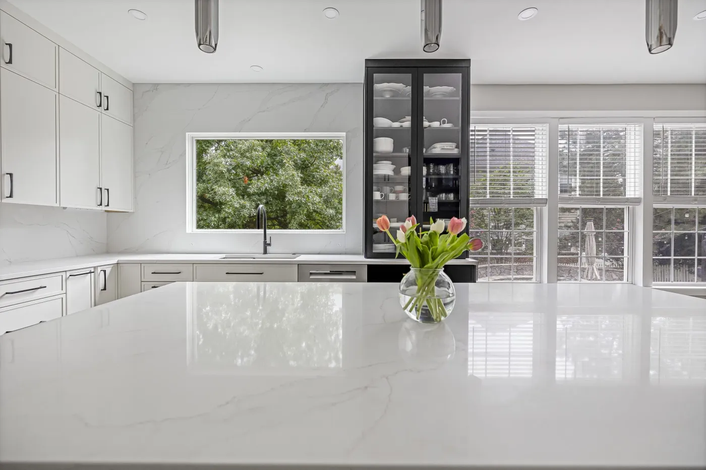 White kitchen with marble waterfall island, pendant lighting and large windows, completed in Northern Virginia